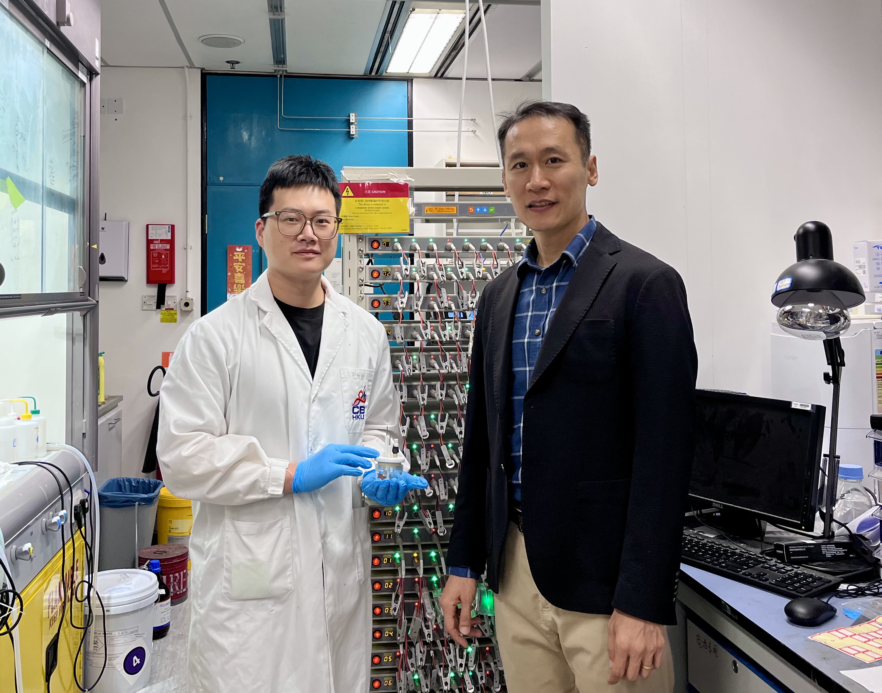 Prof. Yoonseob KIM (right), Associate Professor in the Department of Chemical and Biological Engineering and the study’s corresponding author, and his PhD student YIN Zhuoyu (left), the study’s first author, who is holding an electrochemical cell mold. They are pictured beside a battery cell cycler.